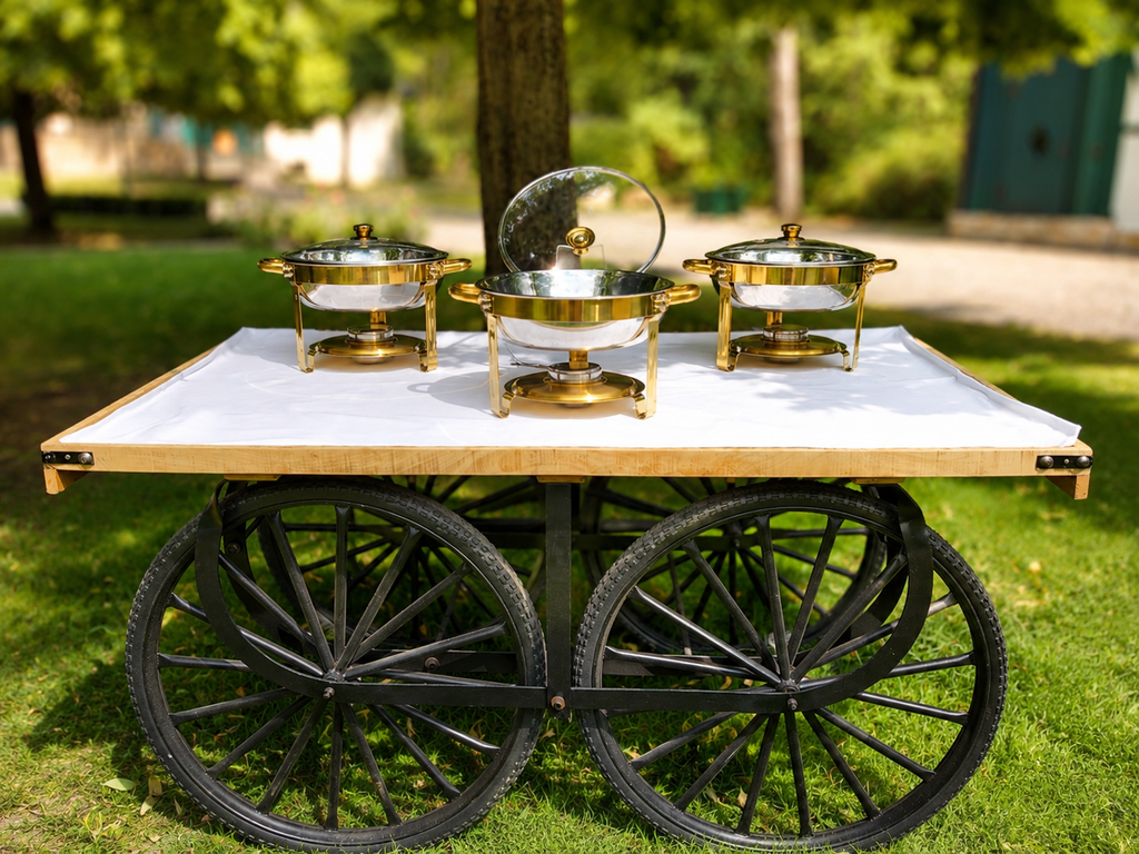 Drei runde goldfarbene Chafing Dishes mit Glasdeckeln auf einem Buffetwagen im Freien