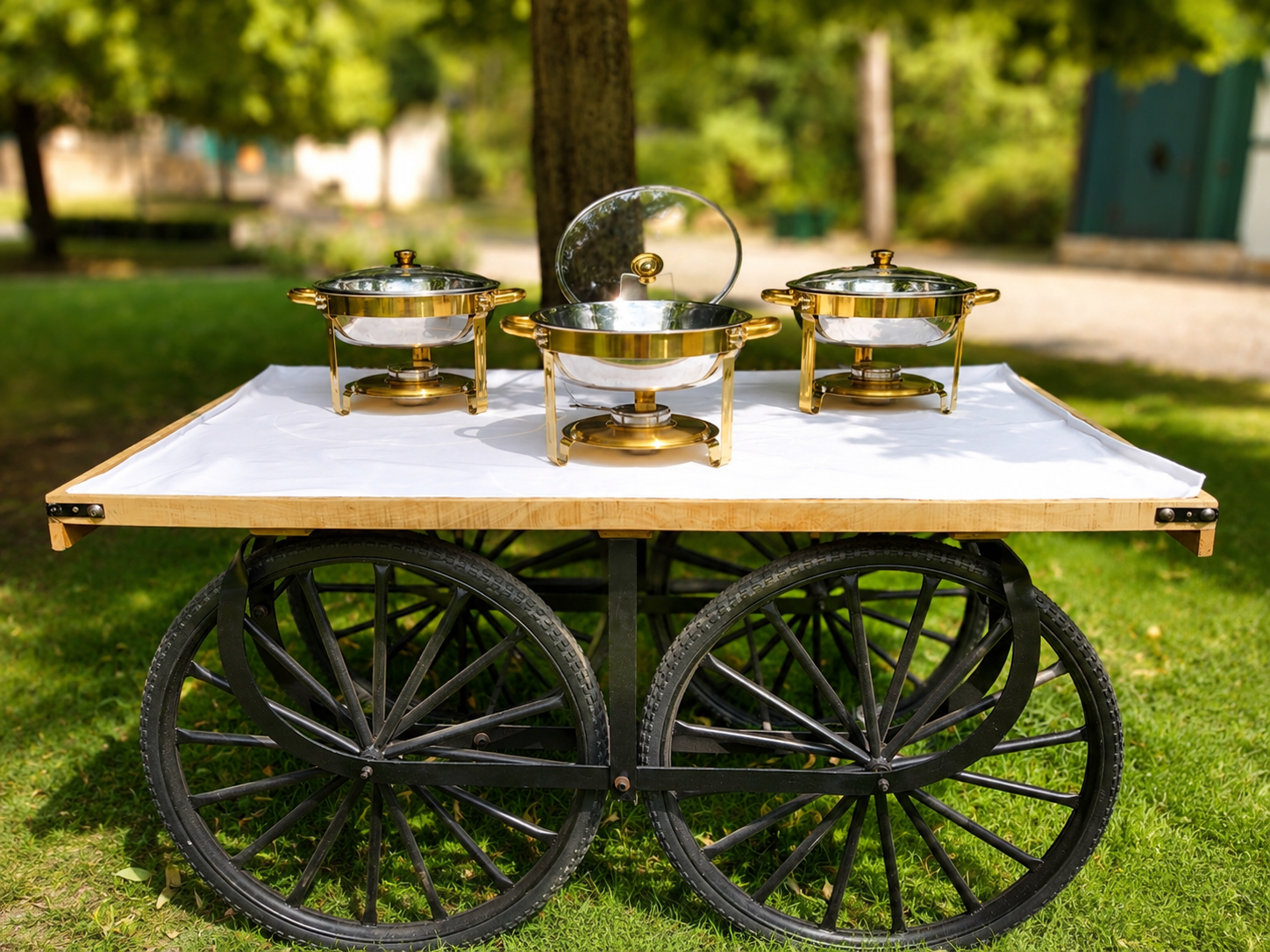 Drei runde goldfarbene Chafing Dishes mit Glasdeckeln auf einem Buffetwagen im Freien