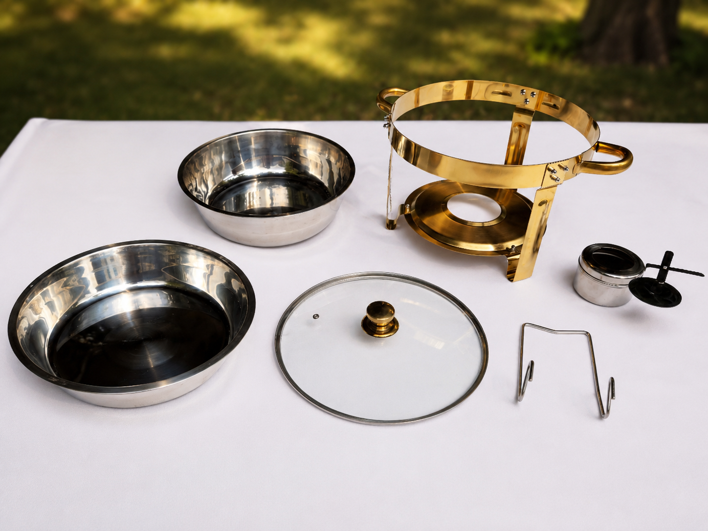 Einzelteile eines runden Chafing Dishes mit goldfarbenem Gestell, Wasser- und Speiseschale, Glasdeckel samt Halterung und Brennpastenhalter